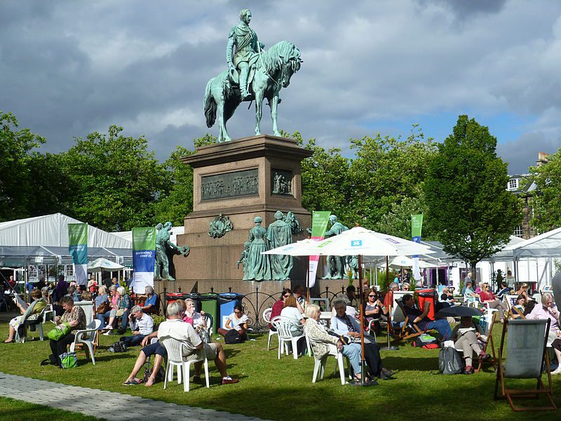 A colourful tent at a book festival, bustling with visitors.